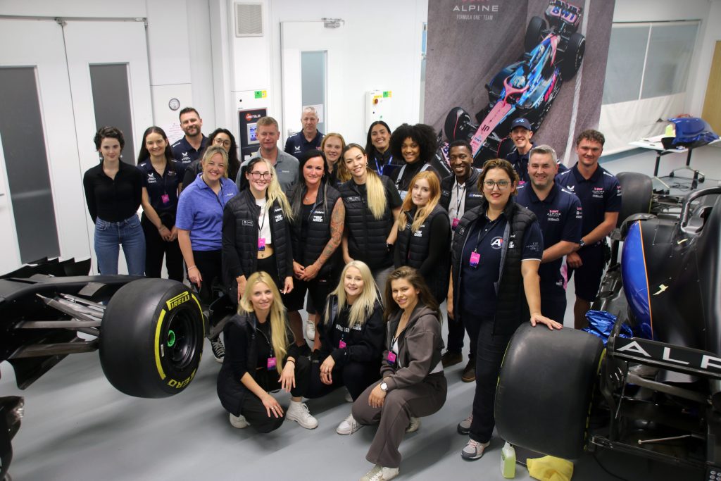 Predominantly female group of car wrappers and engineers grouped around formula one cars at Roland event