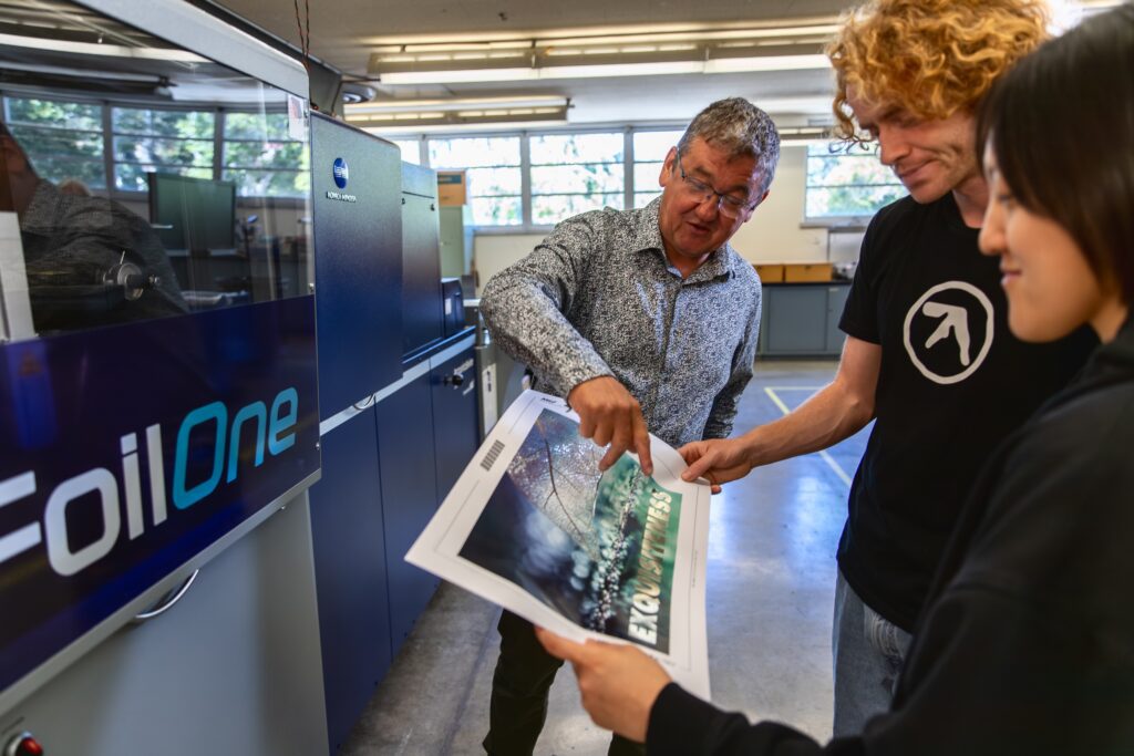 Konica Minolta’s Director of Color Solutions, Dr. Mark Bohan (L), reviews output from the AccurioShine 3600 digital embellishment press with Cal Poly Graphic Communication students Kevin Manni (M) and Anney Haong (R).
