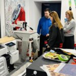 A group of students watches as a garment is loaded onto a digital direct-to-garment printer