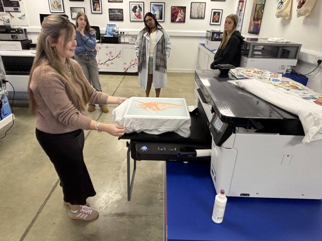 Industry professionals demonstrate a heat press machine to students during a textile printing workshop