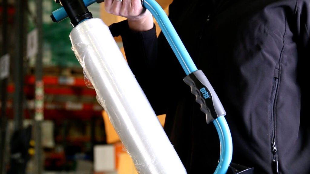 A warehouse operator holding the blue Grip manual stretch film dispenser with a roll of clear film attached