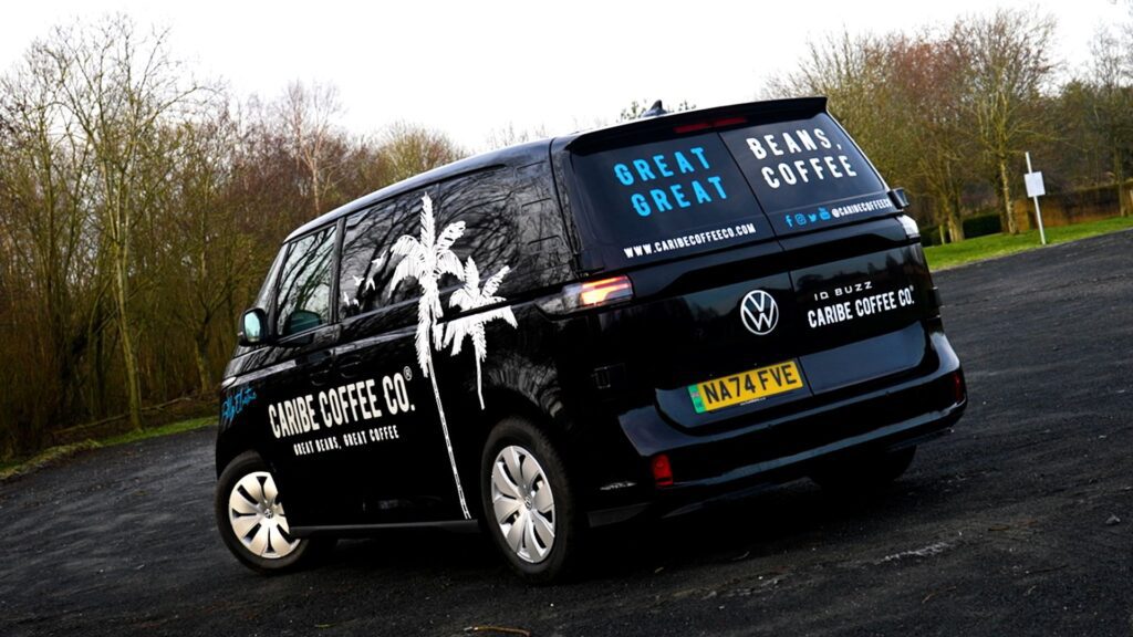 A black VW ID Buzz van with white "Caribe Coffee Co." branding and palm tree graphics parked outdoors