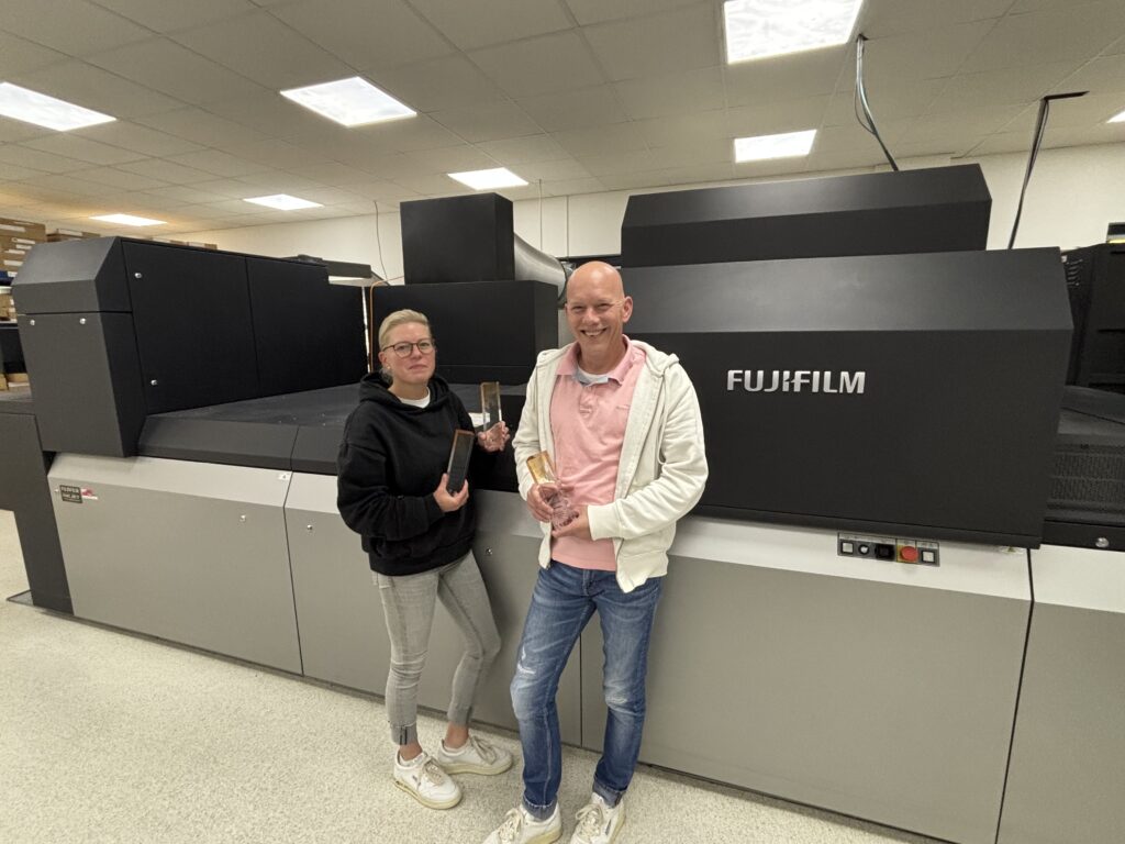 Henning Rose and Sandra Rose standing in front of a Fujifilm Jet Press machine holding award trophies