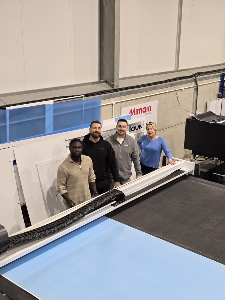 Four members of the Mountain Print team standing next to a large format digital cutting table in a production facility