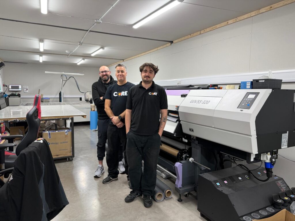 Three members of the Core Exhibitions production team standing next to a Mimaki UJV55-320 large format printer