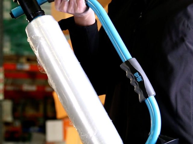 A warehouse operator holding the blue Grip manual stretch film dispenser with a roll of clear film attached