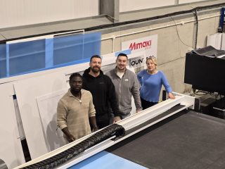 Four members of the Mountain Print team standing next to a large format digital cutting table in a production facility